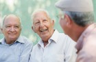 Active retirement, group of three old male friends talking and laughing on bench in public park
